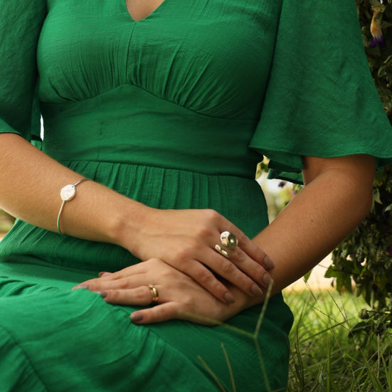 Anel Botão e Palito Orgânico Banhado a Prata na mão de uma mulher com roupa verde e esmalte nude combinando com bracelete