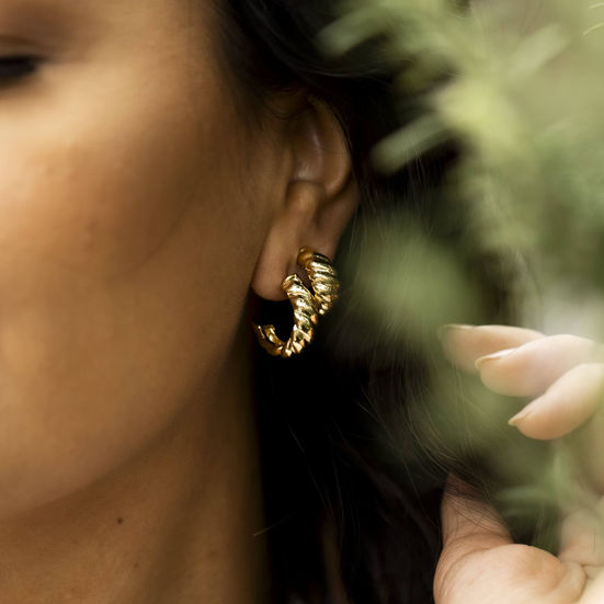mulher usando dois pares de Brincos Meia Argola Croissant Banhado a Ouro 18k com a mão no cabelo