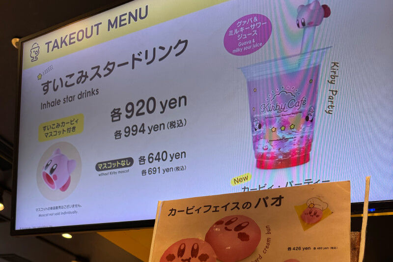 Cafe menu showing Kirby-themed drinks and buns, with colorful graphics. Prices in yen are listed. Bright and playful atmosphere.
