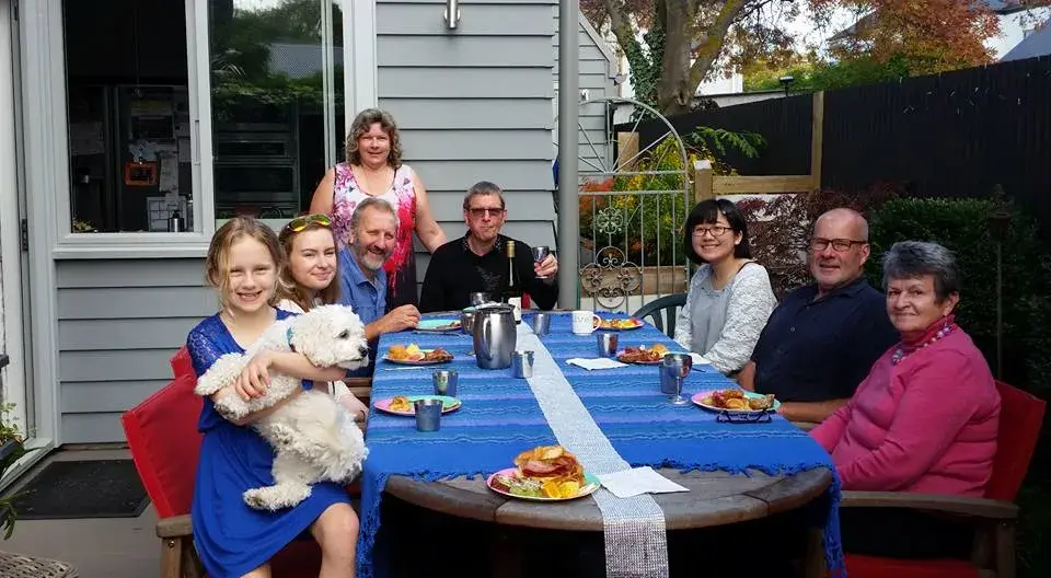 A Japanese exchange student enjoying dinner with her New Zealand host family during a homestay experience.