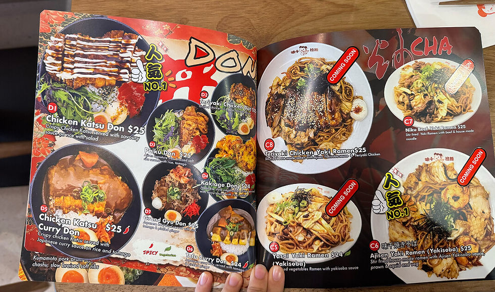 Open restaurant menu showing Japanese donburi and ramen dishes with photos, prices, and red COMING SOON labels on a dark wood table
