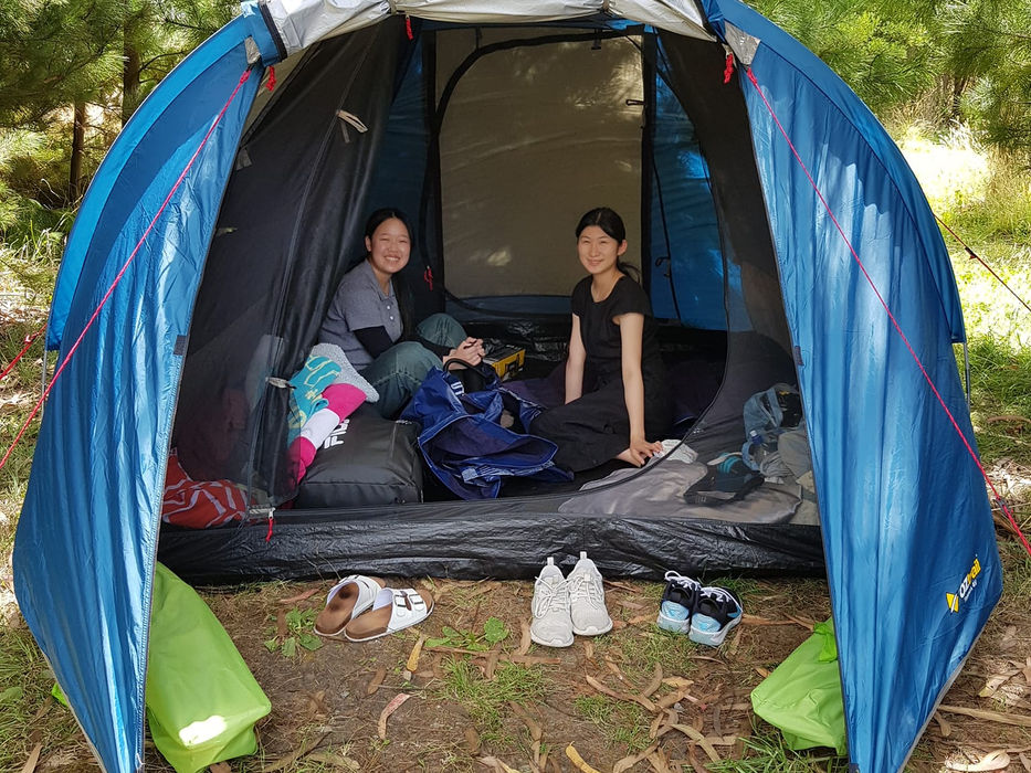 Japanese exchange students relaxing in and around their tents during an outdoor camping trip in New Zealand.