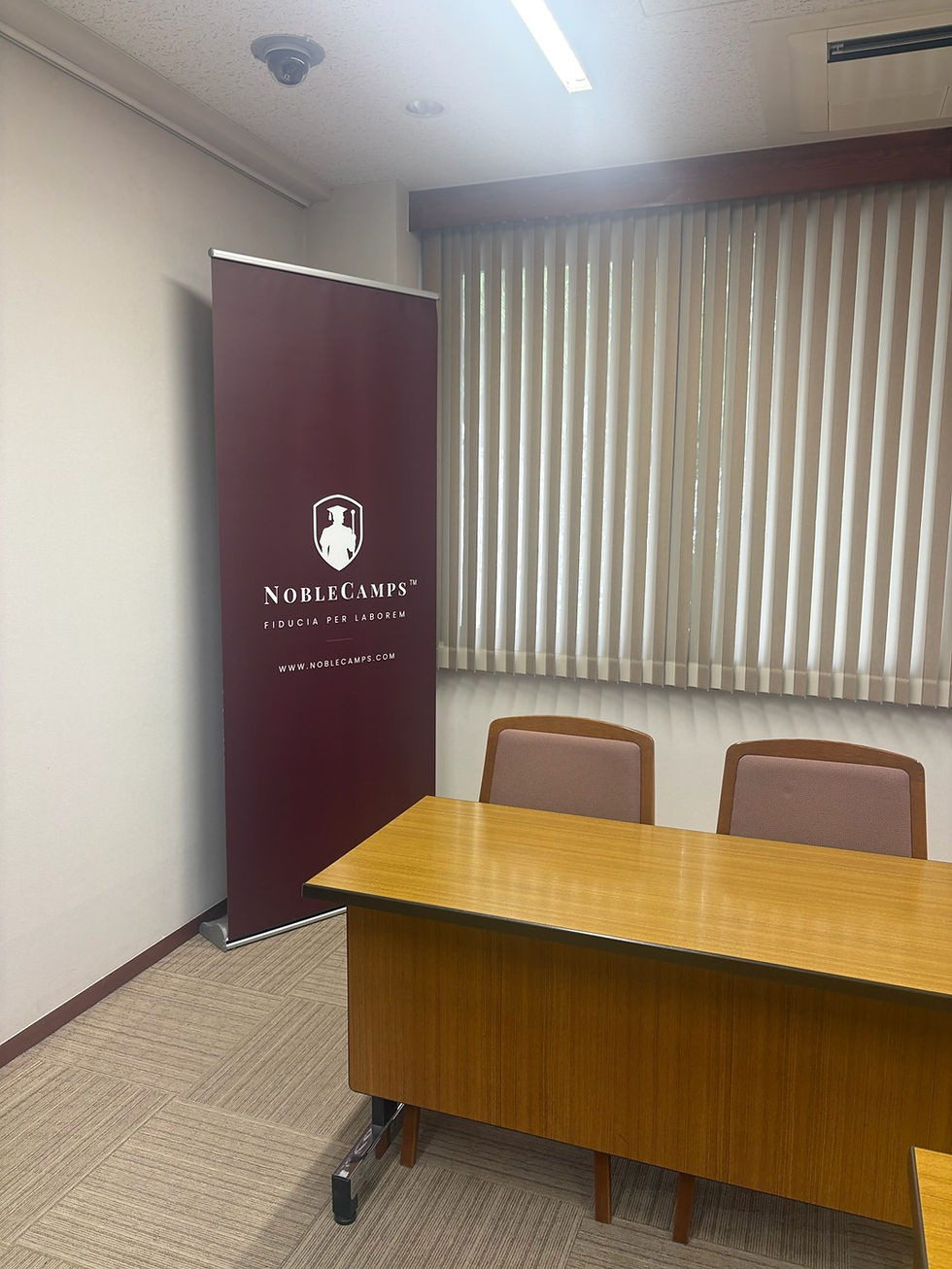 Empty office meeting room with wood table and chairs, maroon NobleCamps banner, blinds, and fluorescent lighting.
