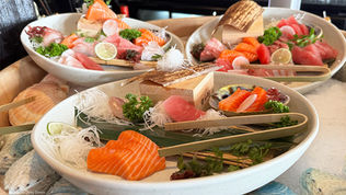 A sashimi platter on crushed ice featuring beautifully arranged slices of tuna, salmon, and white fish, garnished with shredded daikon, shiso leaves, and bamboo trays.