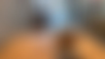 Iced coffee on a wooden table in a cozy cafe with a glass door view of street. A blurred figure stands near the entrance. Warm ambiance.