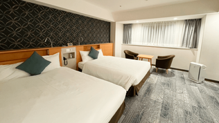 Twin beds, window side table and chairs, and an air purifier creating a relaxing room atmosphere.