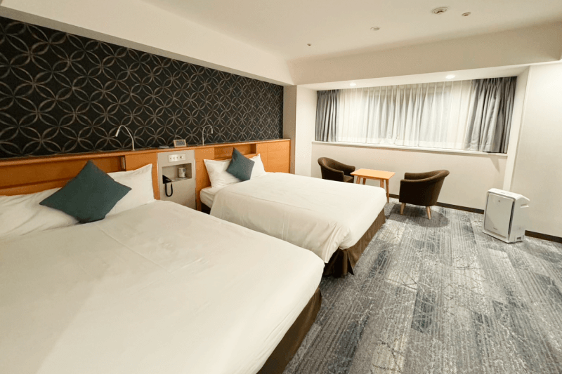 Twin beds, window side table and chairs, and an air purifier creating a relaxing room atmosphere.