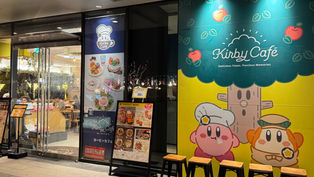 カービィカフェの外観。カラフルな看板にカービィとキャラクターのイラスト。夜で店内に人々が食事を楽しんでいる様子が見える。