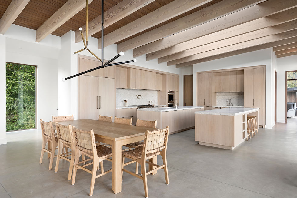 Modern kitchen with light wood cabinetry, quartz island, and exposed wood beam ceiling with skylights.