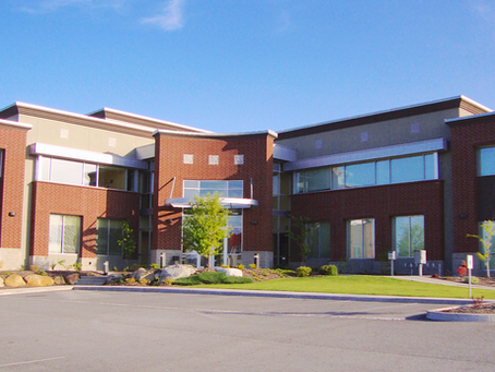 Modern Commercial brick office building with large windows and empty parking lot under a clear blue sky.