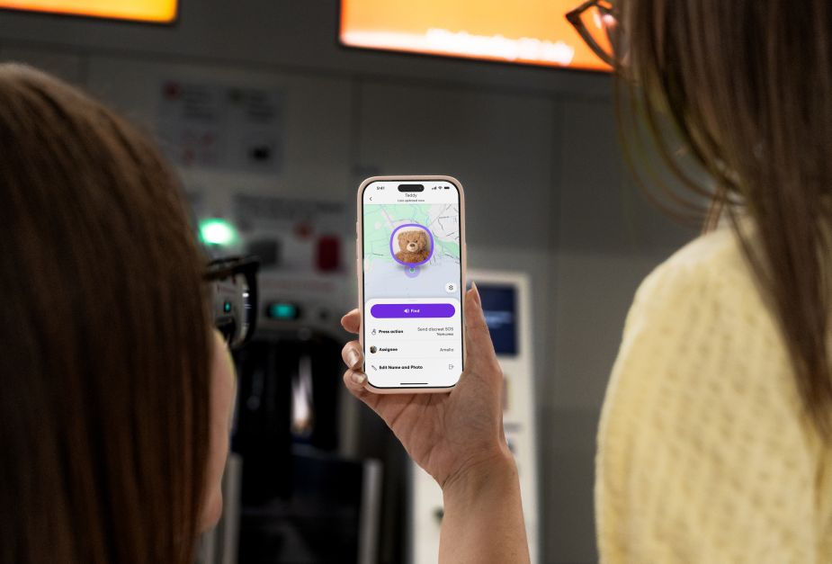 Two people look at a phone showing a teddy bear on a map in the Find app indoors.