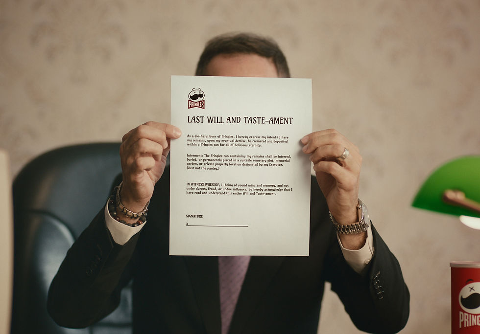 Man in a suit holds a Pringles Last Will and Taste-ament sheet in an office, with a green lamp and can in the background.