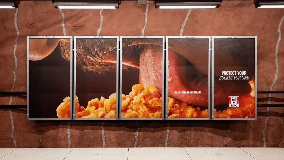 KFC ad on five wall panels shows a mouth eating fried chicken; text reads Protect your bucket for one by any means necessary.