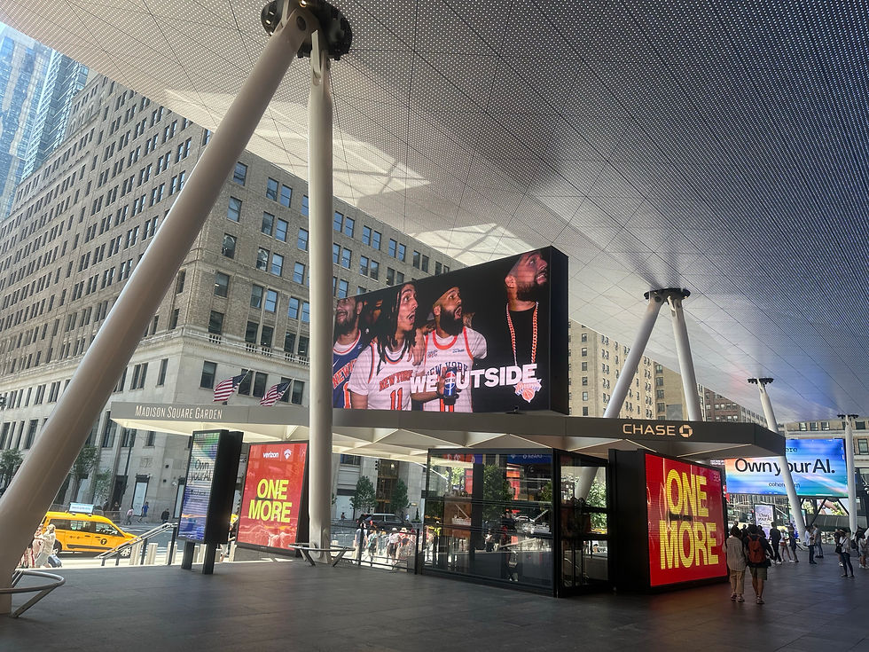 Outside Madison Square Garden under a perforated canopy, giant LED screens show ONE MORE and WE OUTSIDE as people walk by.