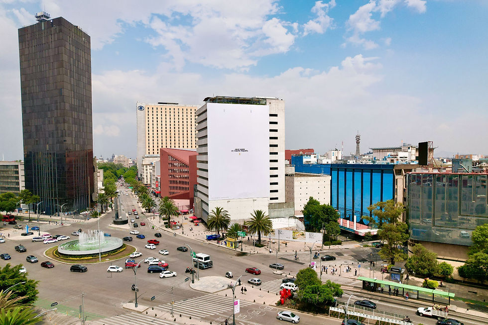 Busy city intersection with a fountain, tall modern buildings, palm trees, and a bright blue sky; white building has tiny text.