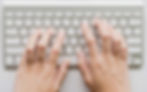 Picture of a white keyboard and a person typing on it