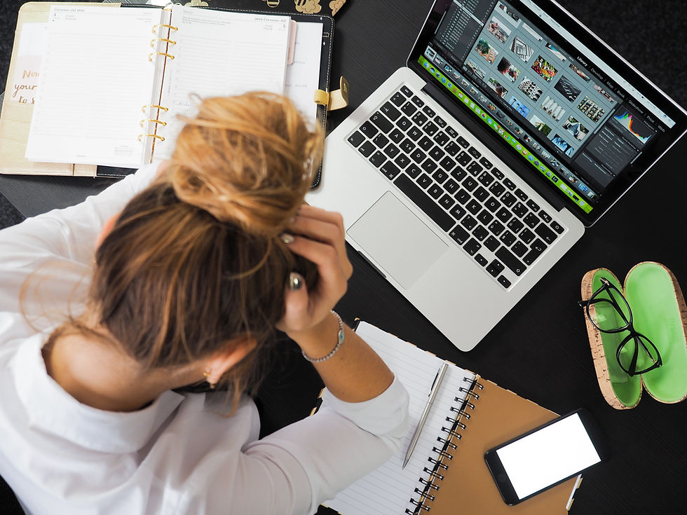Photo of a woman with her head in her hands looking down at her laptop and notebooks.