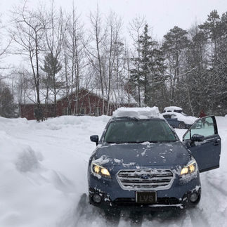 A blue Subaru Outback is parked in front of a snowy cabin in northern Wisconsin.