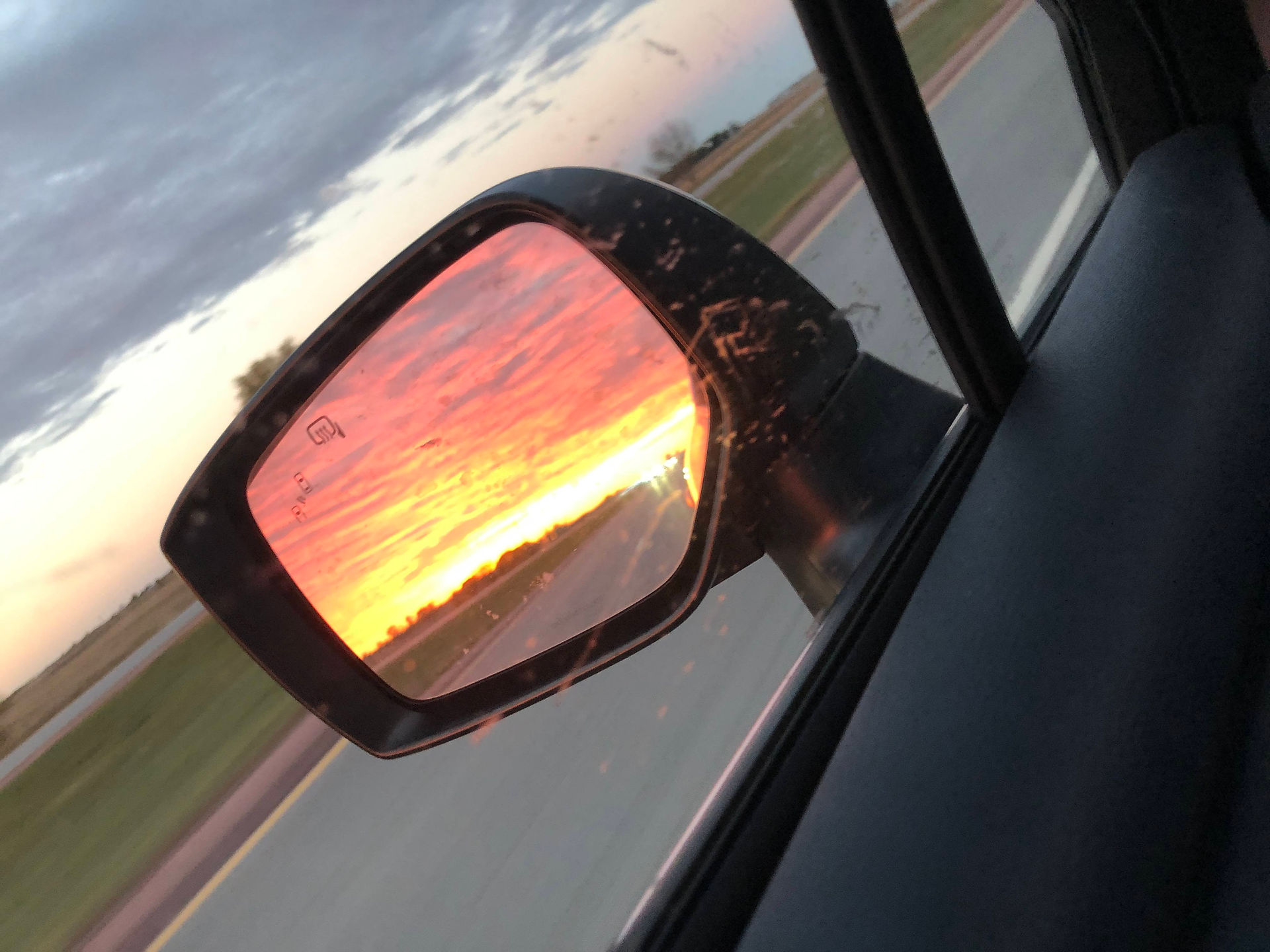 The side mirror of a. Subaru Outback showing a blazing bright pink sunset. USA