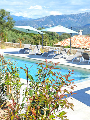 Piscine extérieure avec chaises longues, parasols et montagnes en arrière-plan.