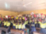 School girls in yellow and black school uniforms hold up menstrual hygiene kits in a classroom
