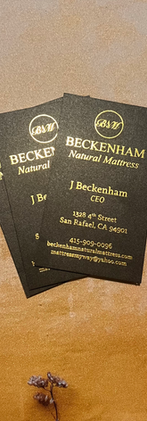Three black and gold Beckenham Natural Mattress business cards rest on a golden surface.