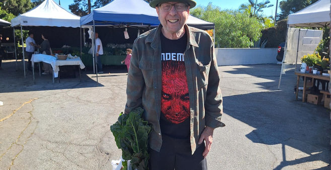 Jonny smiles at farmers market carrying produce, red graphic tee.