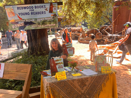 Book signing booth under redwoods with sign for young readers; Lori Peelen displays Tree Home Book