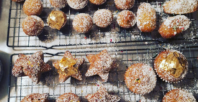 Various donuts dusted with powdered sugar, arranged on two wire cooling racks.