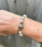 a handmade boho-style stretch bracelet displayed on a wrist with a distressed wood fence background. The bracelet displays 8m
