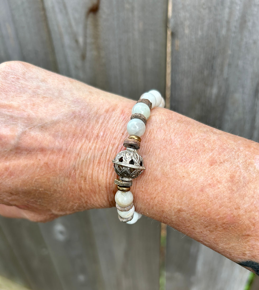 a handmade boho-style stretch bracelet displayed on a wrist with a distressed wood fence background. The bracelet displays 8m