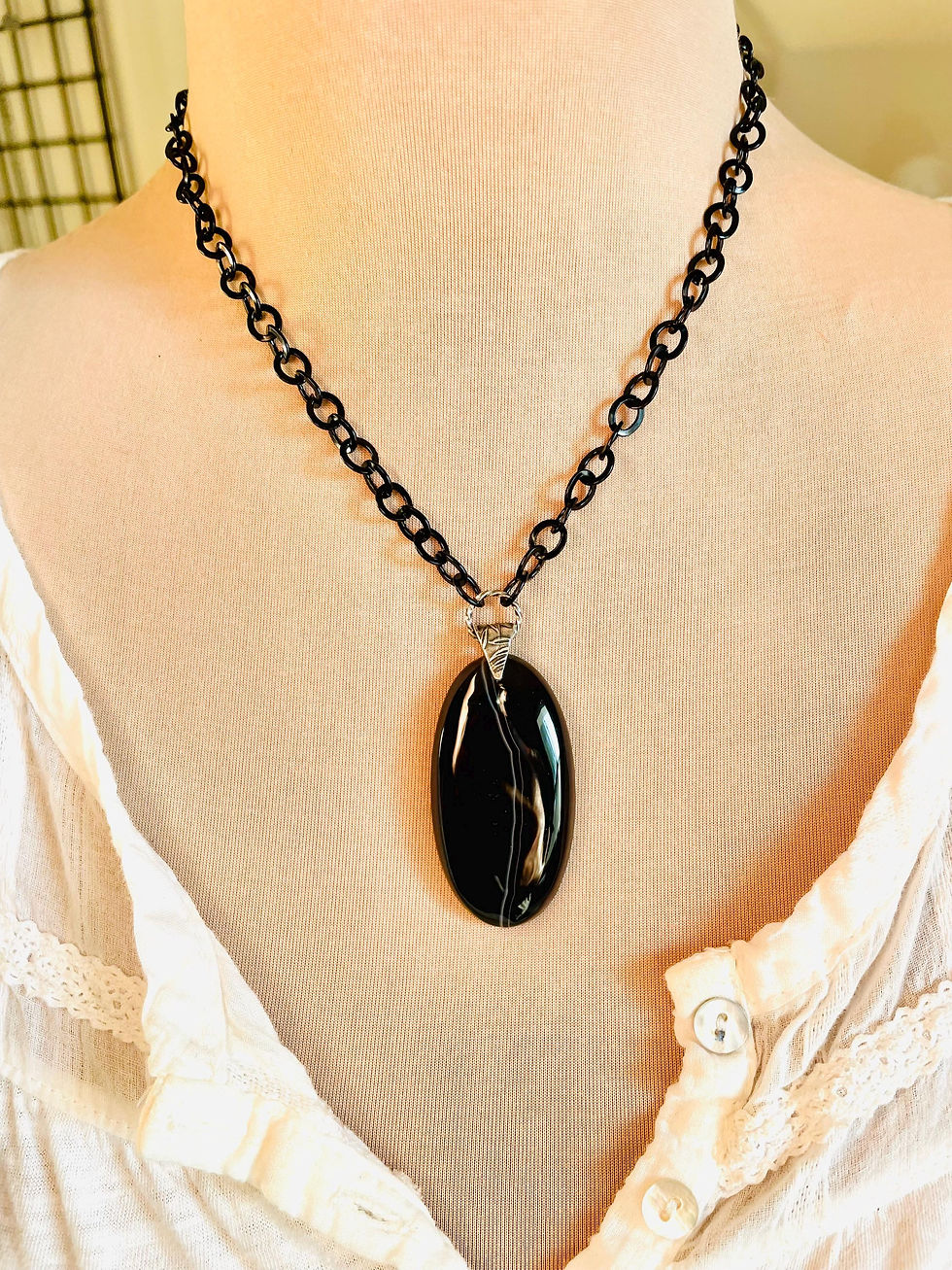 Thumbnail: A black banded Agate pendant necklace with a black chain. The pendant is oval shaped.