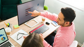 attractive-man-pointing-computer-screen-business-presentation-while-sitting-office-profess