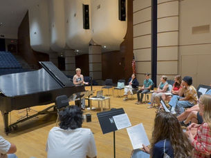 Students in University Concert Hall with guest lecturer and open grand piano