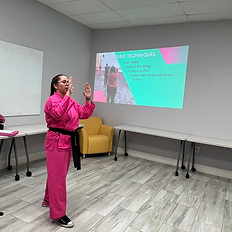 Elicia Ybarra teaching a Pretty Hands, Hard Punches self defense empowerment class, demonstrating safety and awareness skills in front of a projected slide.