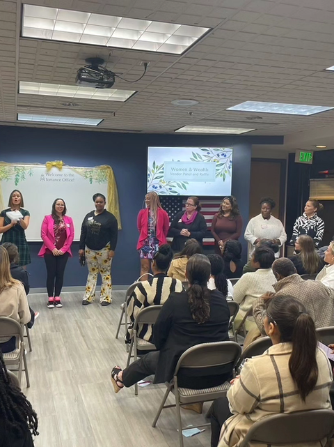 A panel of women, including [Your Name] in a pink blazer, standing in front of an audience at the Women & Wealth Panel, focused on empowering women through knowledge and confidence