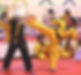 Martial artist in a yellow uniform performing a high kick toward a partner during a training drill in a dojo
