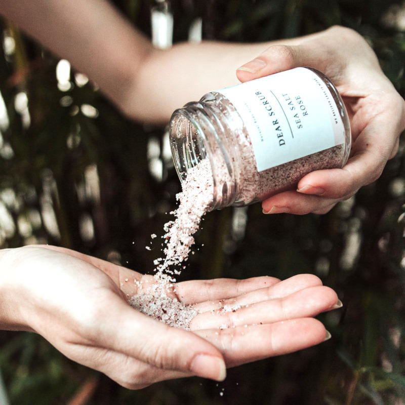 Nahaufnahme: Zwei Frauenhände, die linke Hand hält ein Glas mit gefülltem Salz und schüttet dieses in die rechte Hand.