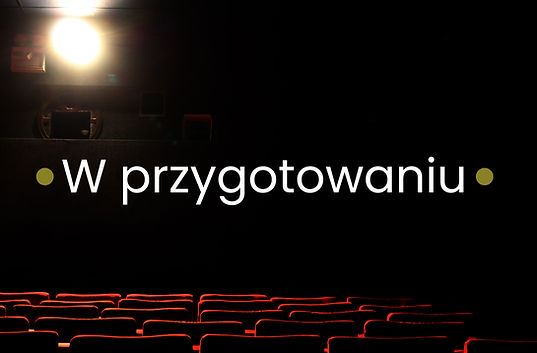 Napis “w przygotowaniu”. Białe litery na czarnym tle widowni teatru. W lewym górnym rogu widać światło reflektora. Na dole czerwone krzesła widowni. Po dwóch stronach napisu - zielone kropki. Zapowiedź nowego spektaklu dla dzieci w naszym repertuarze.