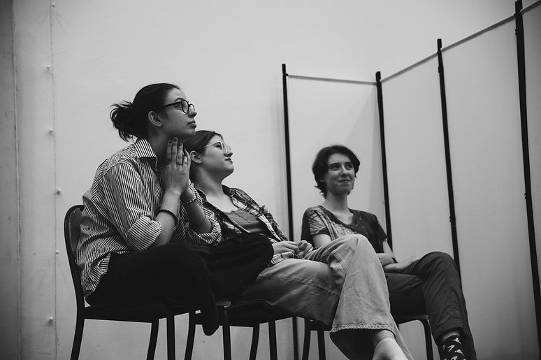 Czarno - białe zdjęcie. Trzyosobowa grupa młodzieży siedzi i słucha z zainteresowaniem trenera umiejętności społecznych na warsztatach teatralnych.To kreatywne zajęcia dla młodzieży prowadzone przez Czułą Fundację.