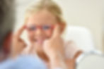 A young child having prescription glasses put on her face