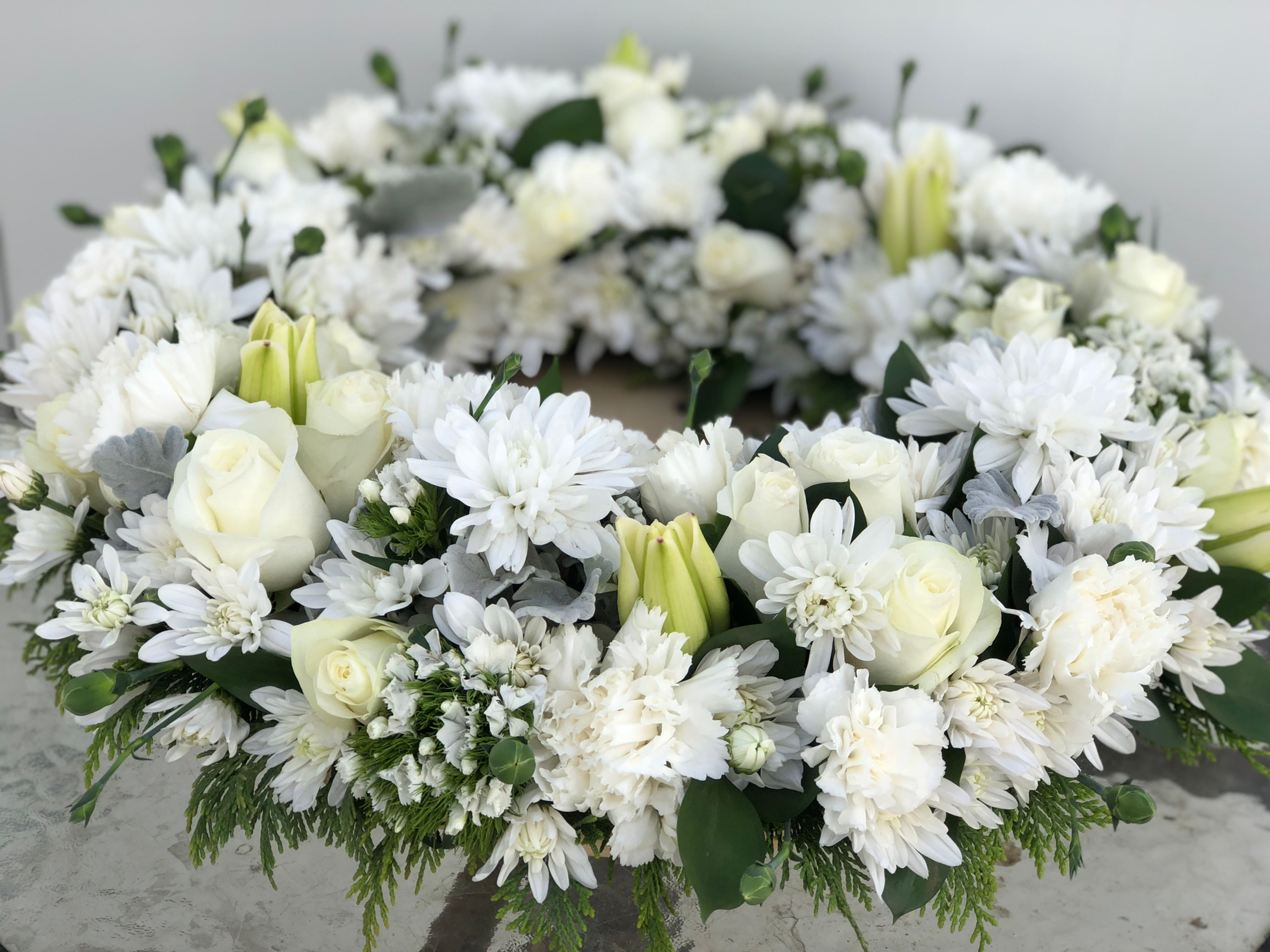 White sympathy wreath made up of white flowers such such chrysanthemum, roses, carnations, baby's breath