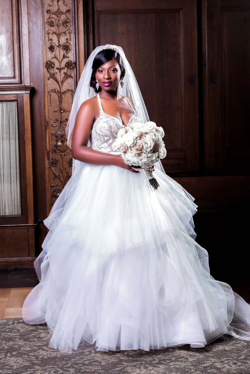 A bride in a white wedding dress, holding a bouquet smiling for a photo, radiating happiness on her special day.