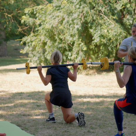 Two women performing barbell lunges in Battersea Park outdoor PT class