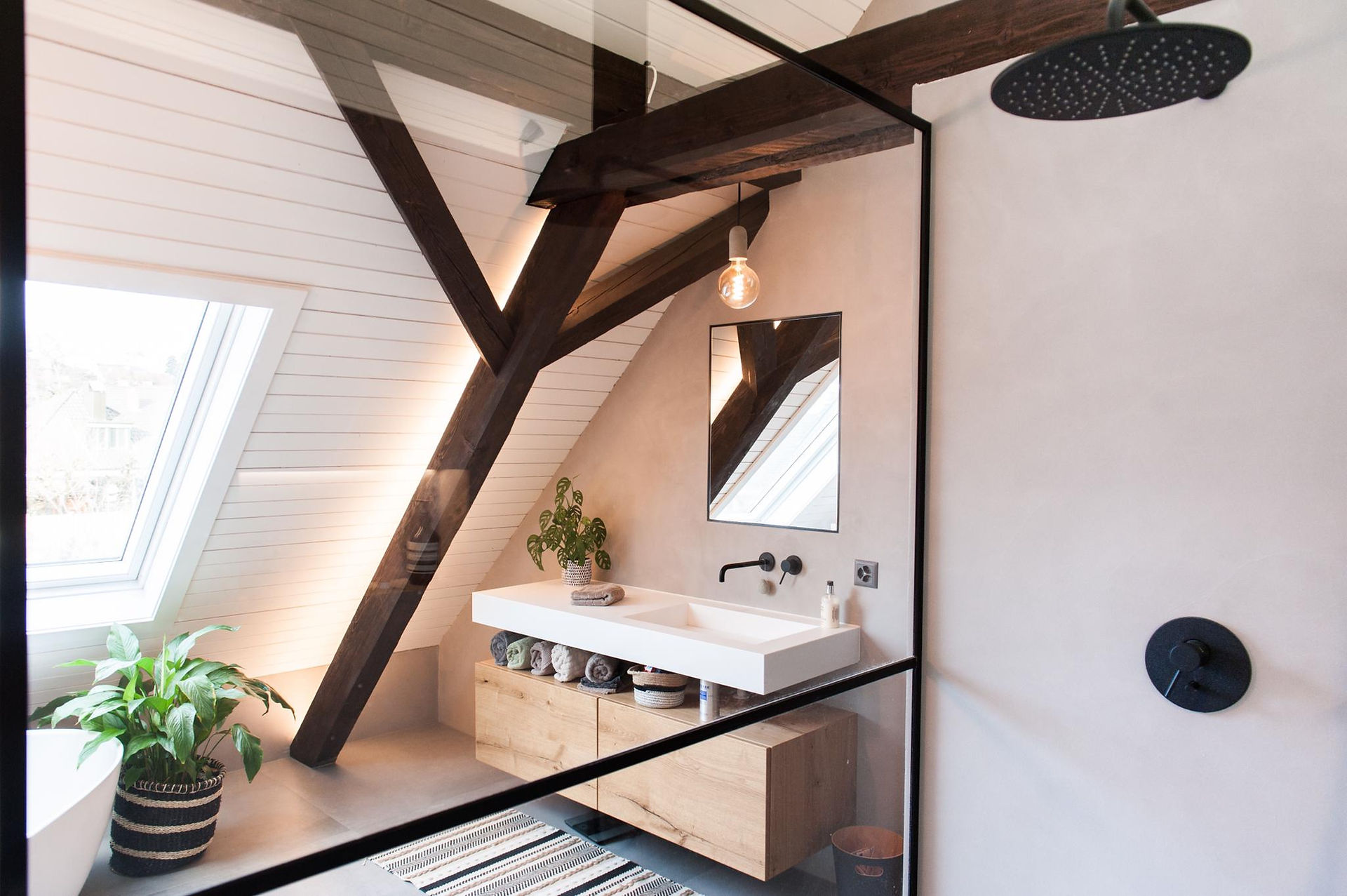 Stylish bathroom with exposed wooden beams, a wall-mounted sink on a wooden vanity, pendant lighting, and a large mirror beneath a sloped ceiling.