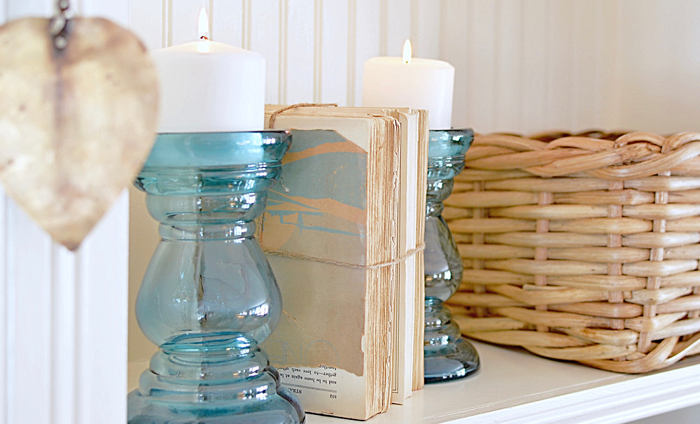 Vintage books with blue glass candlesticks and basket on shelf.
