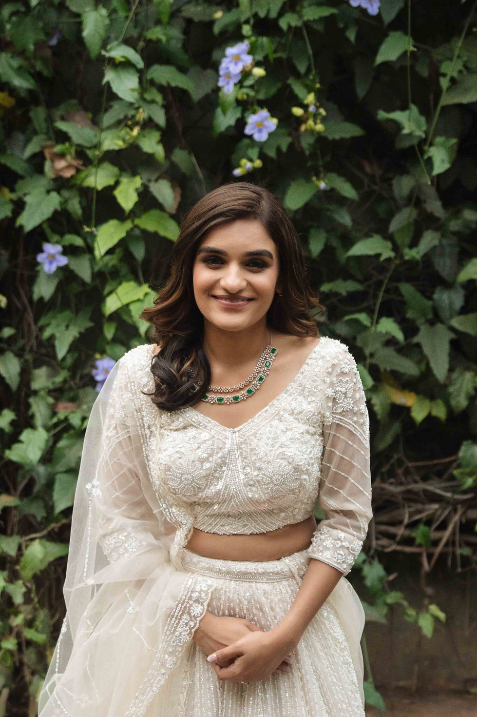 Woman in white outfit, smiling, surrounded by greenery.