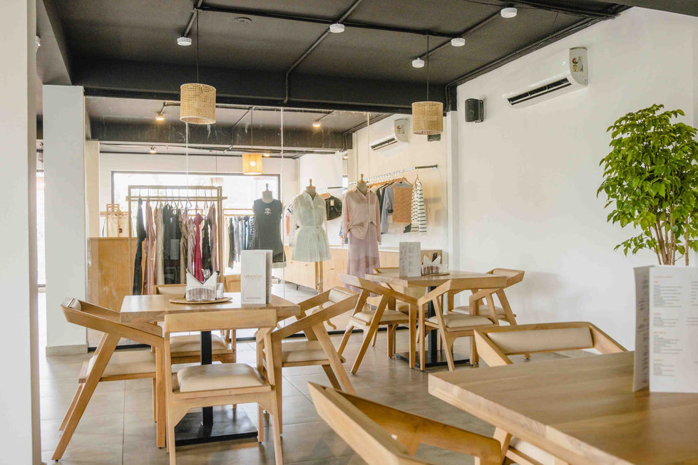 Modern cafe with wooden tables and chairs, clothing displayed.