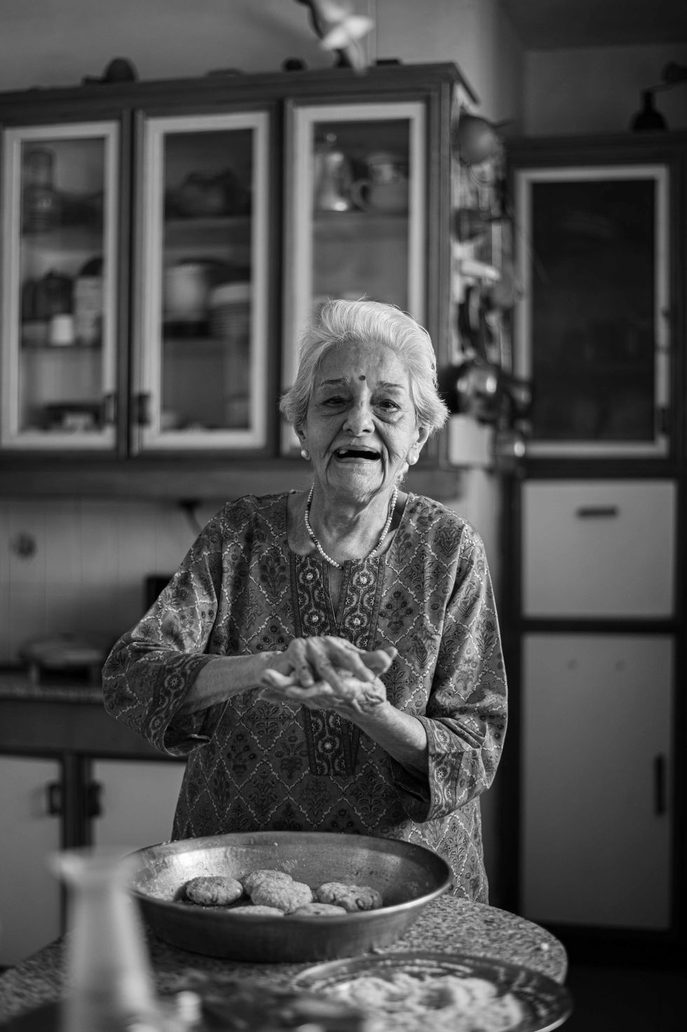 Elderly woman smiling in a kitchen, black and white.