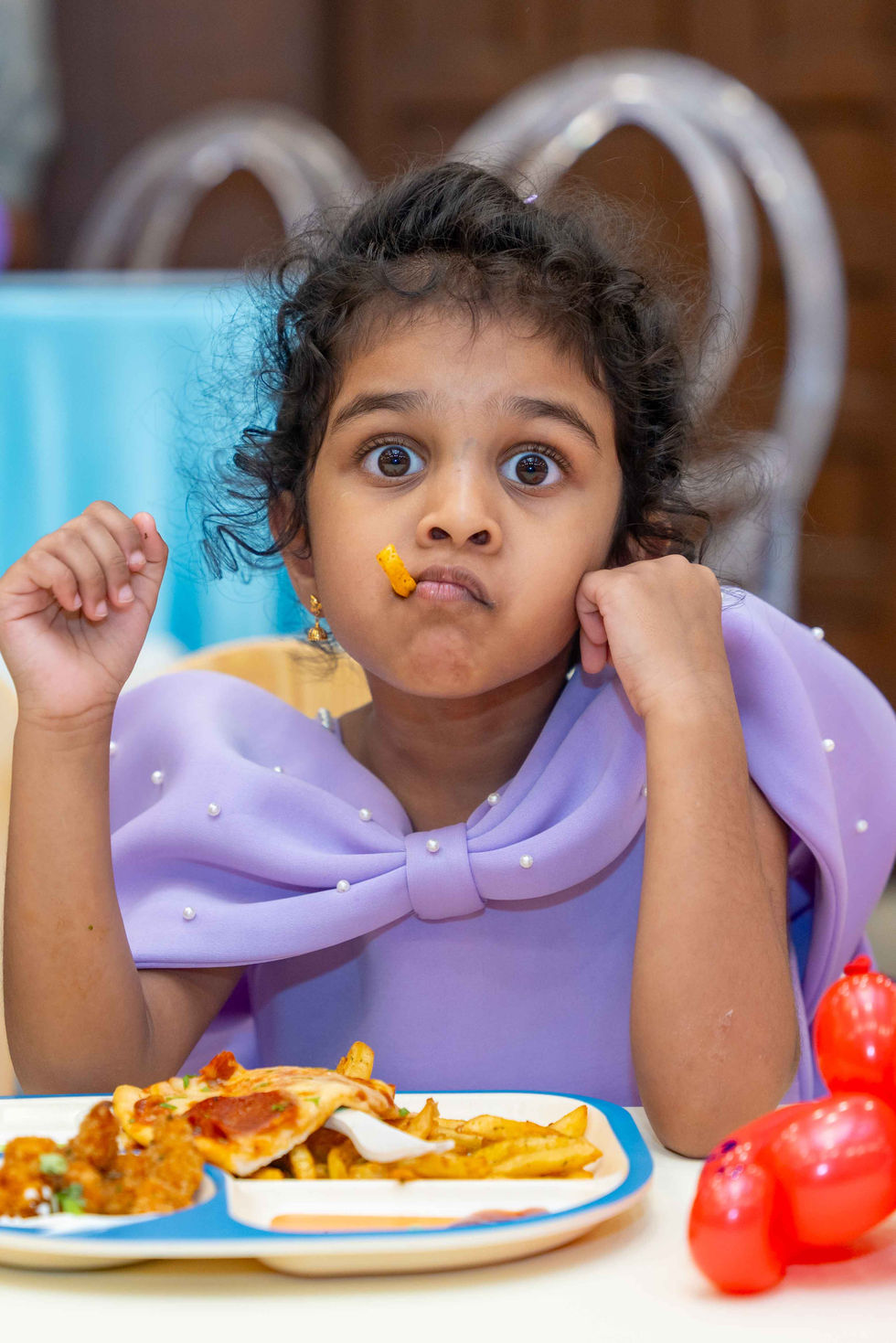 Child eating with surprised expression, wearing purple outfit.